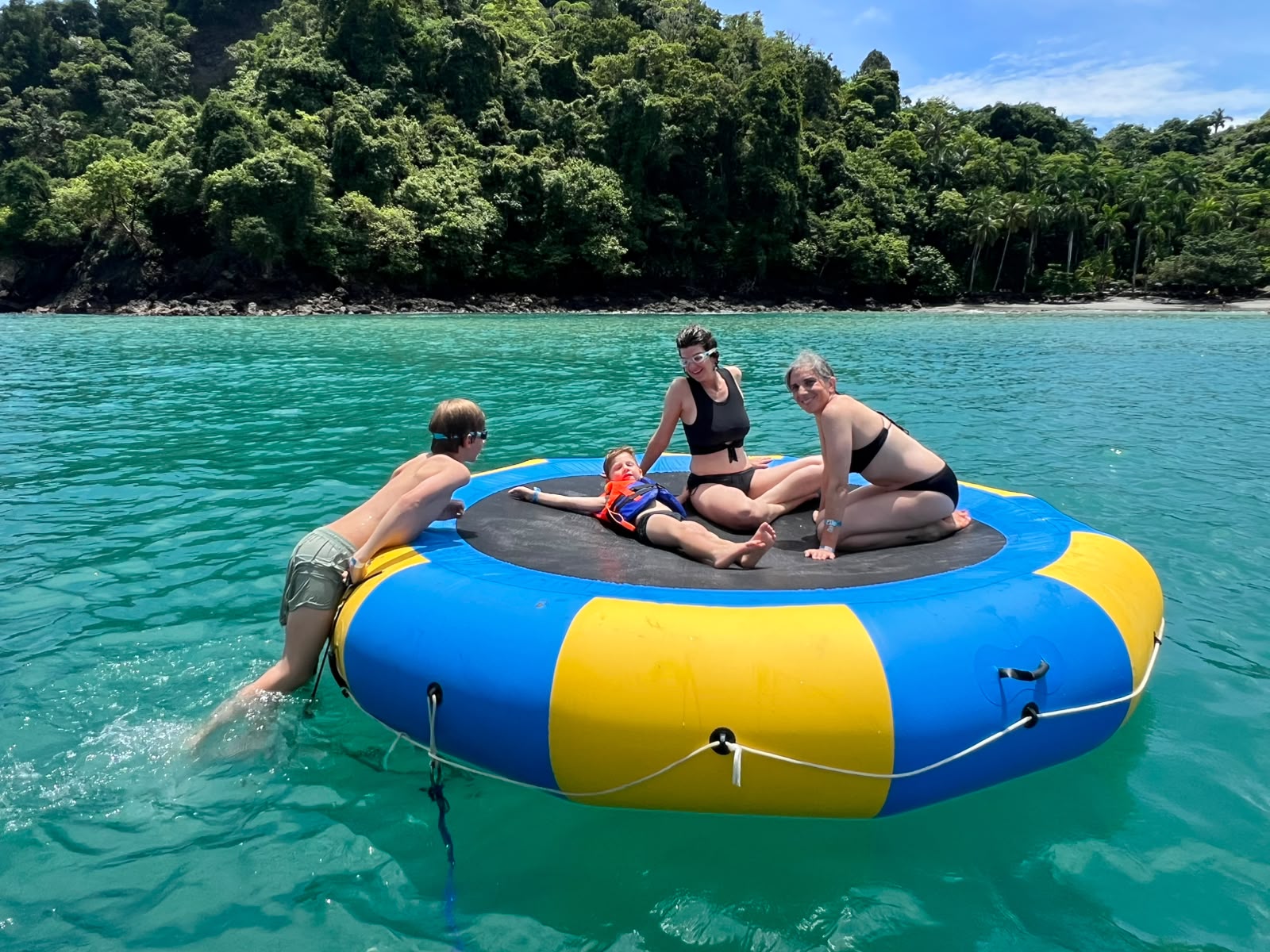 A family laughing and waving from the water trampoline in a turquoise cove in Manuel Antonio